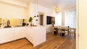 Une cuisine moderne avec des meubles blancs, une table à manger en bois et des chaises, ainsi qu’une grande fenêtre ornée de rideaux légers.