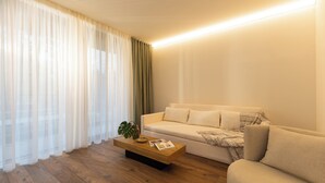 Un salon moderne avec une table basse en bois, un canapé beige et des rideaux légers.