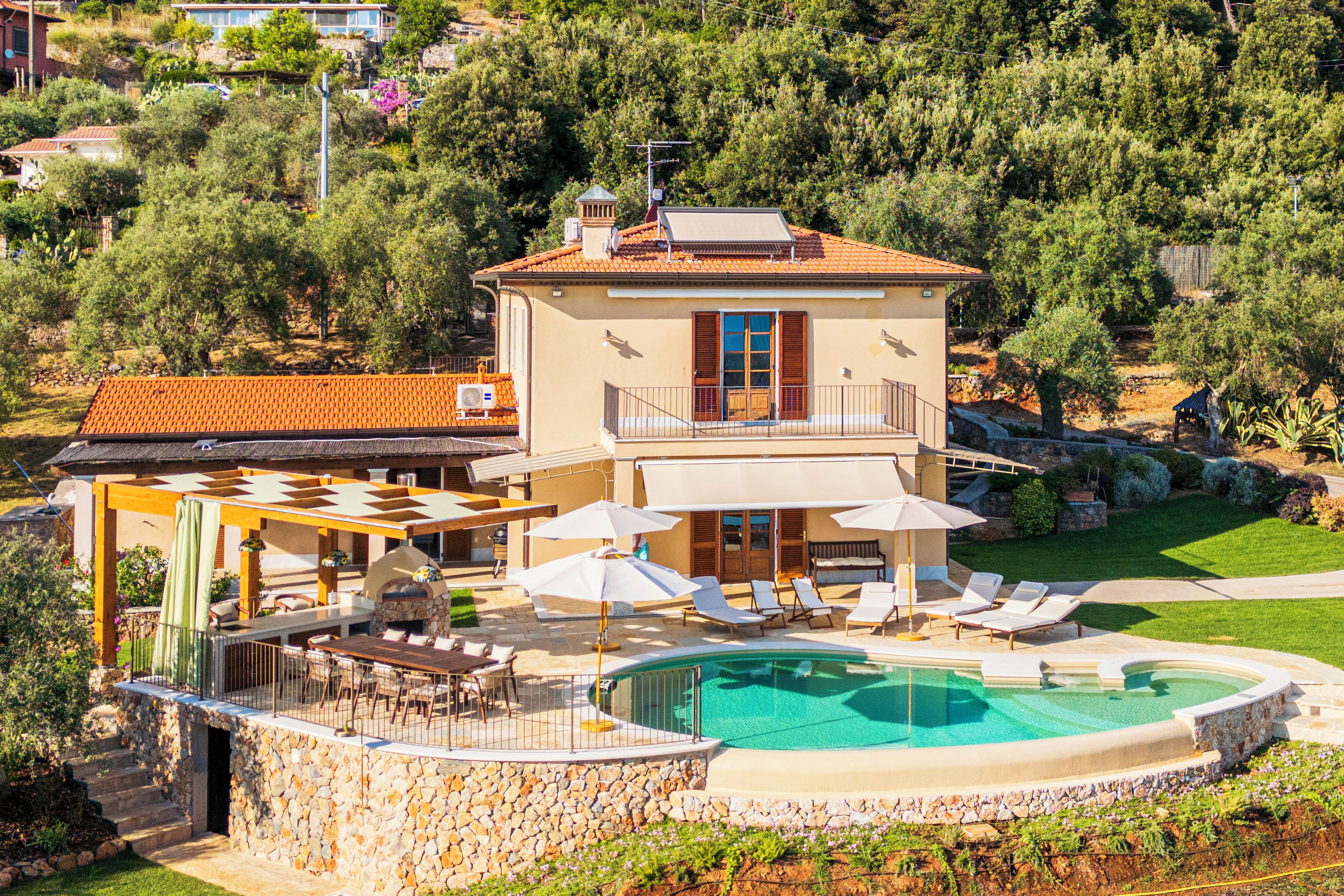 A two-story villa with a swimming pool, outdoor seating, and a stone wall.