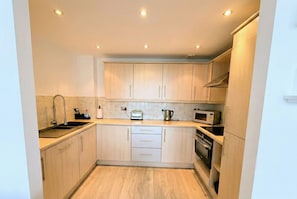 A compact kitchen with light wood cabinets, a built-in oven, a microwave, and a toaster. - Kew Connection -
Relax in this light airy river view apartment. (Brentford)