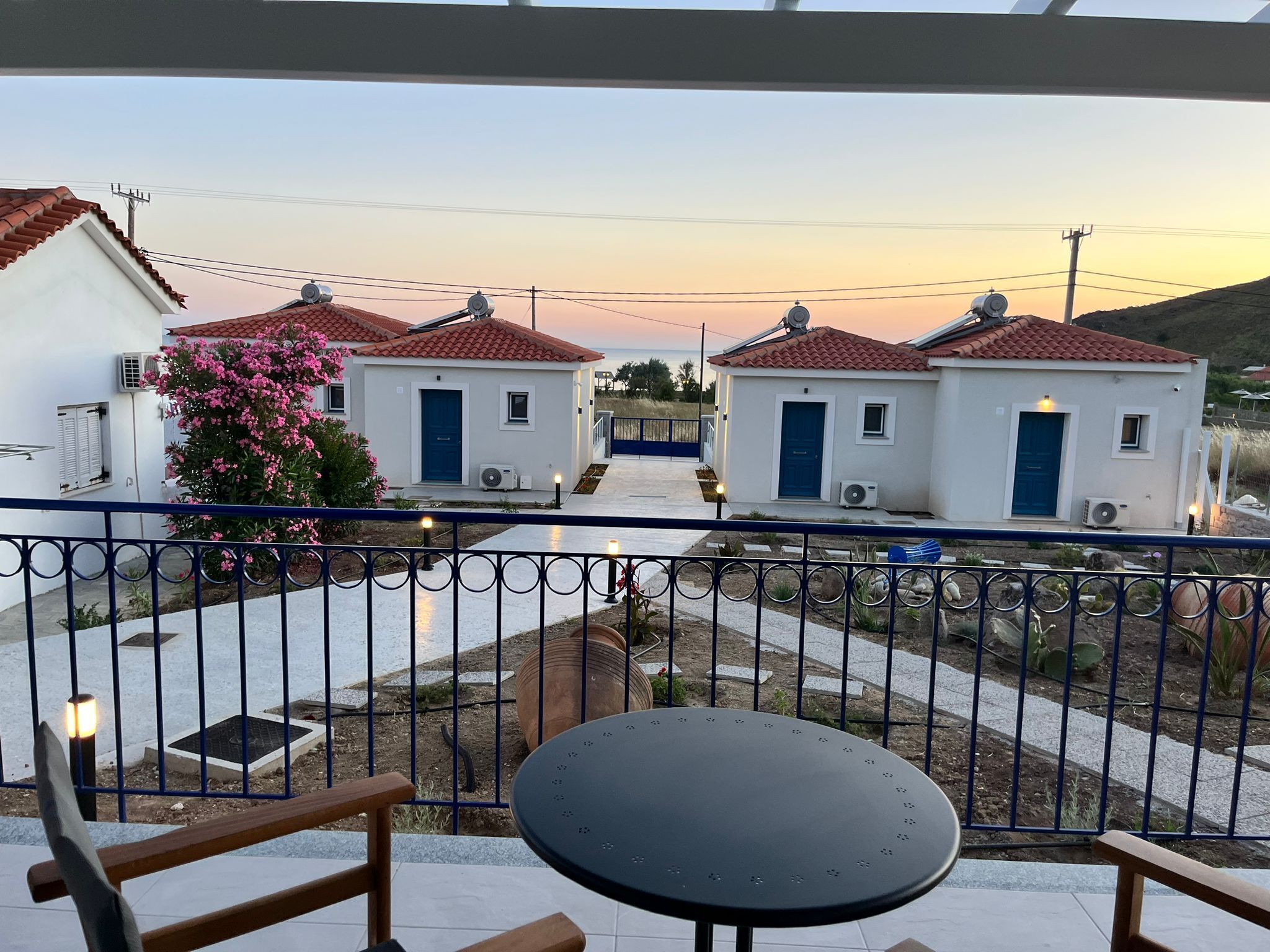 Un balcon avec une table et des chaises, donnant sur une cour intérieure où se trouvent deux bâtiments blancs aux toits rouges.