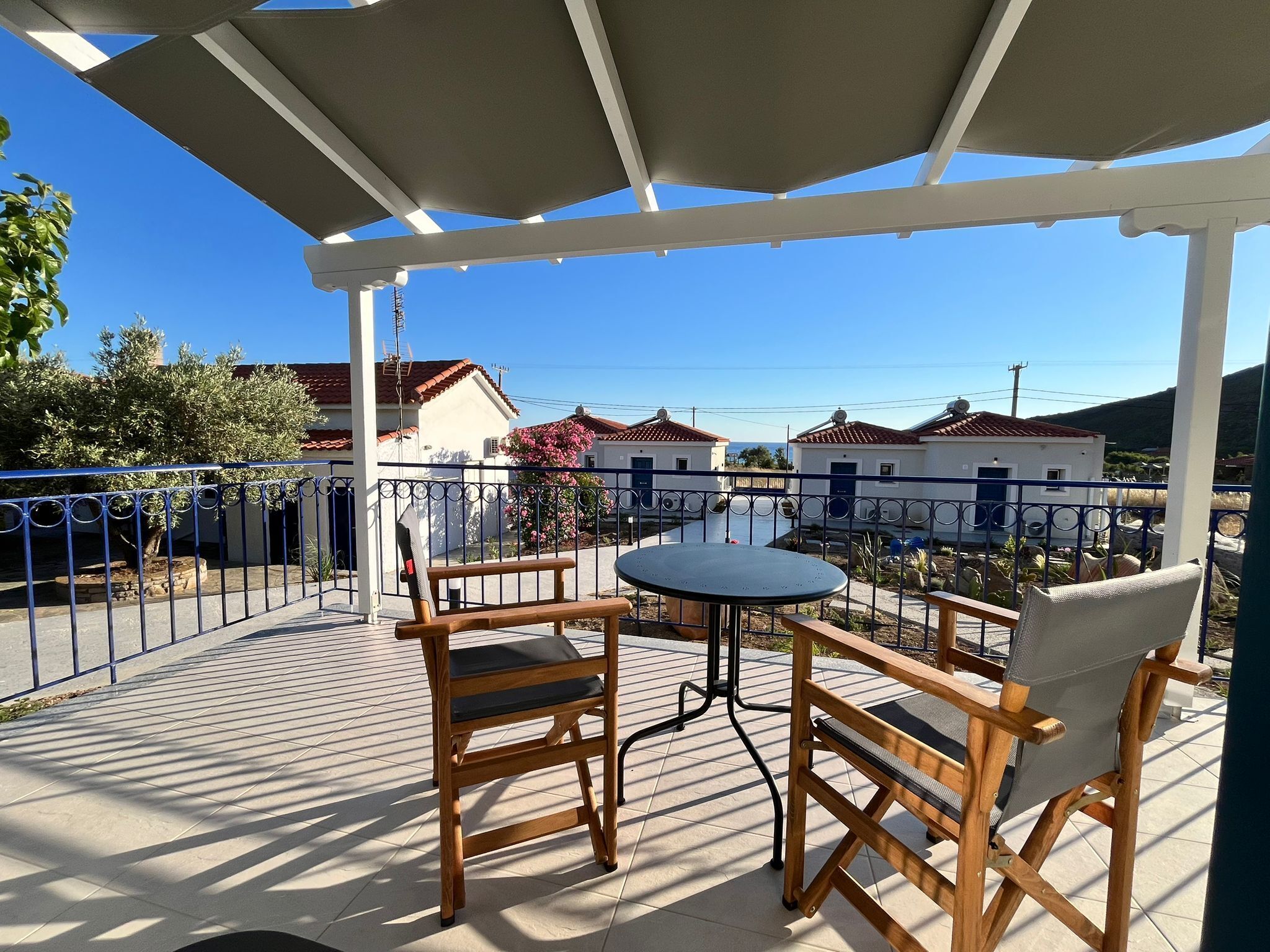 Un patio techado con una mesa y sillas, piso de baldosas y vista a casas al fondo.