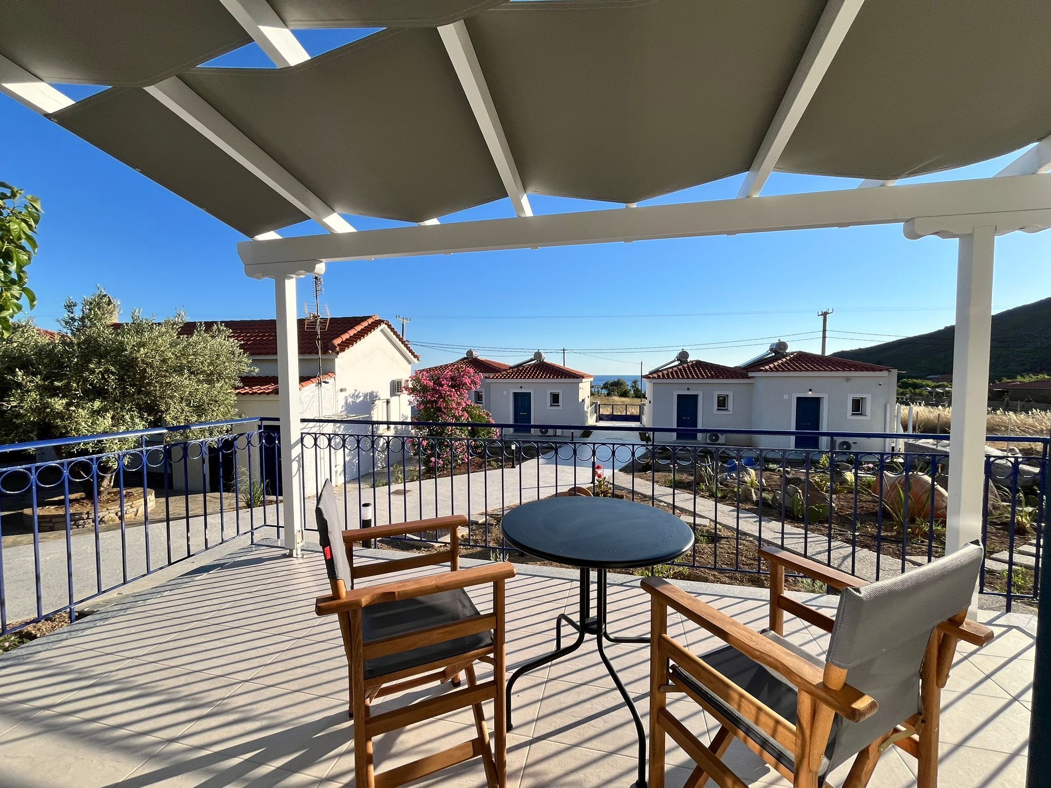 Un espace extérieur abrité, avec une table et des chaises, d’où l’on peut admirer des maisons en arrière-plan, et une clôture en métal.