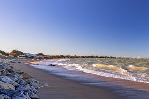 Une plage avec des vagues, une côte rocheuse et une vue lointaine sur des bâtiments.