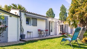Una casa de un solo piso con un patio, una mesa pequeña, sillas y una silla azul para el jardín.