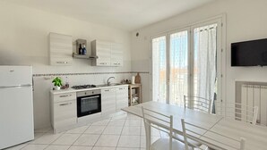 A modern kitchen with a dining area, white cabinetry, and a flat-screen TV mounted on the wall. - P081 - Porto Recanati, new three-room apartment with balcony (Porto Recanati)