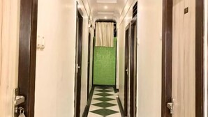Ein Hotelgang mit Schachbrettmuster auf dem Boden, Holztüren und einer grünen Wand am Ende.