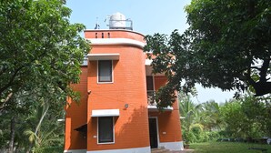 Un bâtiment de forme cylindrique, fait de briques, avec un toit plat, entouré d’une végétation luxuriante.