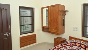 Une chambre avec une armoire en bois, un lit recouvert d’une courtepointe à motifs, une fenêtre avec une grille en métal et une porte.