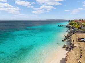 A beach with clear turquoise waters, a pier, and a building with a red roof in the background. - Stylish 2-bedroom vacation home in Belnem, Bonaire—near beaches, dive spots & restaurants. (Belnem)
