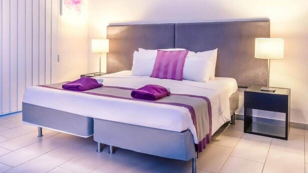 Ein modernes Hotelzimmer mit einem großen Bett, zwei Nachttischen und einem Beistelltisch.