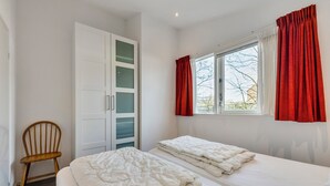 Une chambre avec deux lits, une armoire, une chaise et une fenêtre avec des rideaux.