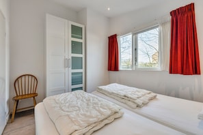 Een slaapkamer met twee bedden, een kledingkast, een stoel en een raam met gordijnen.