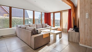 Un vaste espace de vie doté de grandes fenêtres, d’un canapé d’angle, d’une table basse et d’un mur décoratif en bois.
