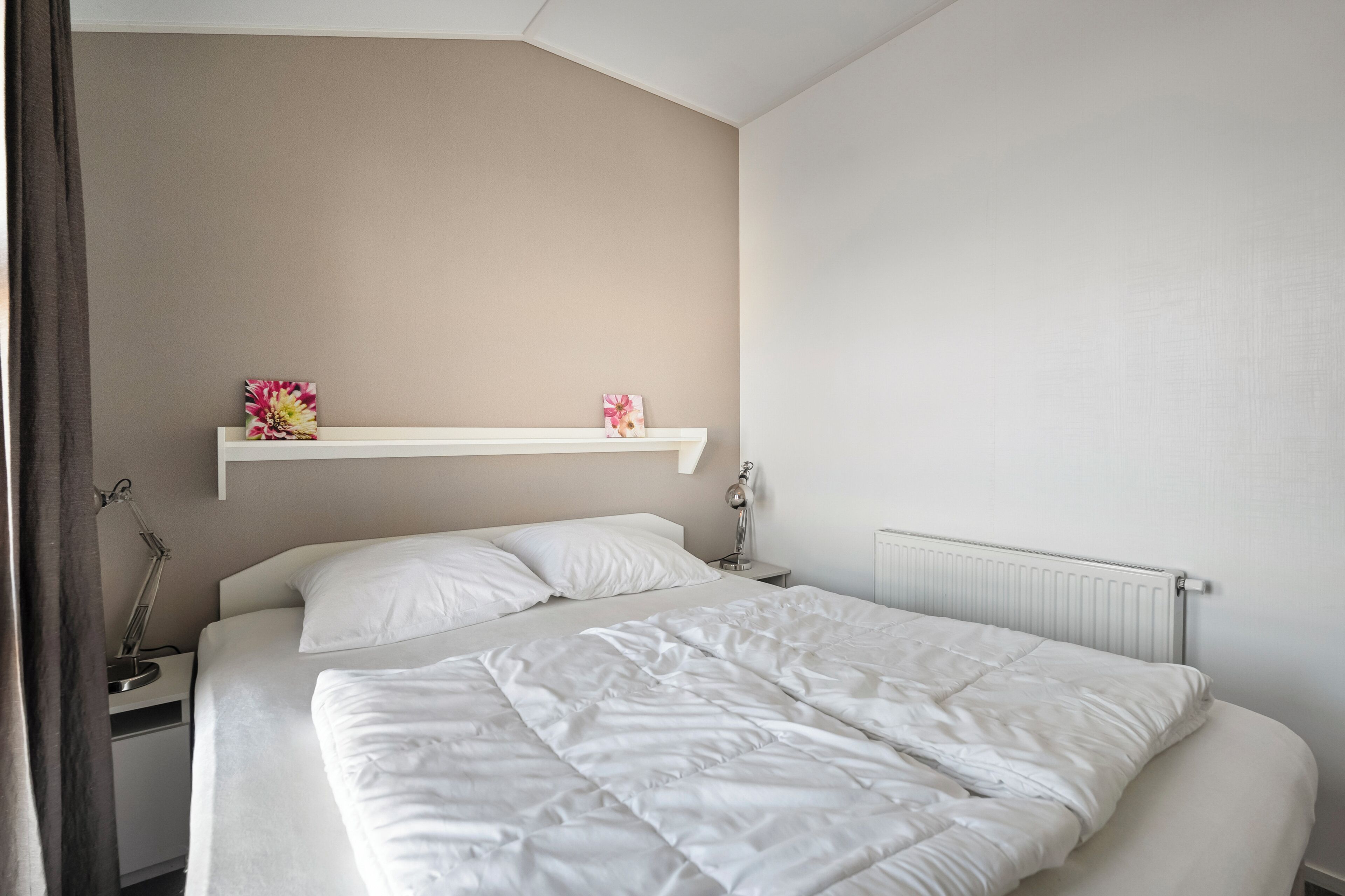 Una cama bien hecha con ropa blanca, una lámpara de noche y una mesita de noche blanca con lámpara.