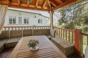A covered outdoor seating area with wicker furniture and a wooden table, overlooking a house and trees. - Villa 'La Rosa De Los Vientos' with Pool and Jacuzzi in the Sierra de Guadarrama (Los Ángeles de San Rafael)