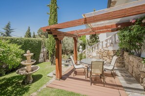A patio with a wooden pergola, a stone wall, and a round table with chairs.
