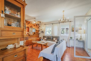 A cozy living room with a sofa, a wooden cabinet with figurines, a chandelier, and a dining table.