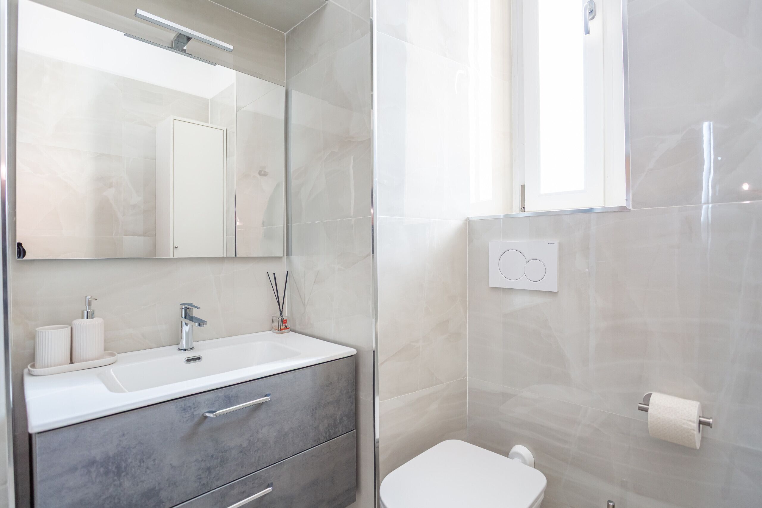 A modern bathroom with a white sink, mirror, and toilet.