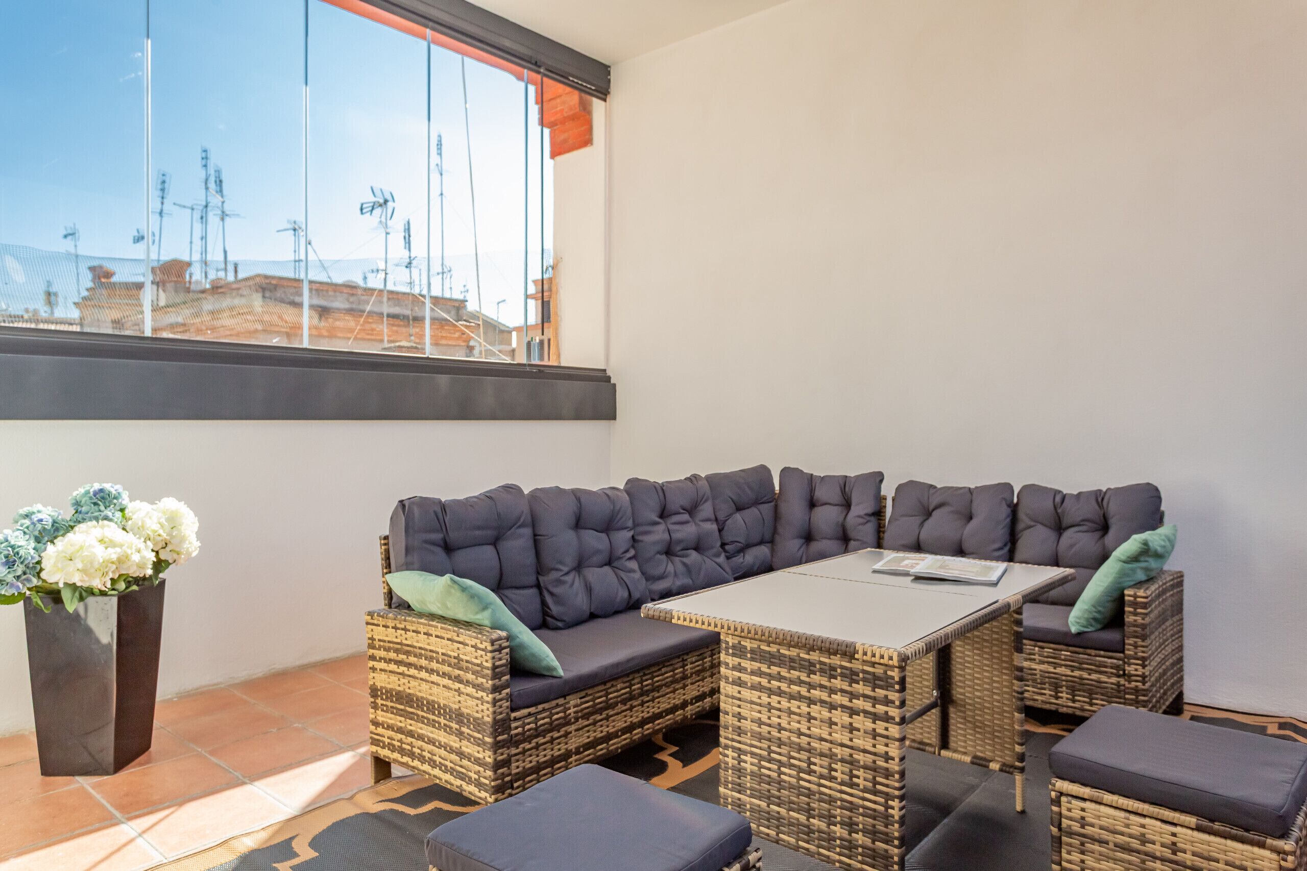 Un espace de détente extérieur moderne, avec un canapé confortable et des poufs, une table rectangulaire et une plante en pot.
