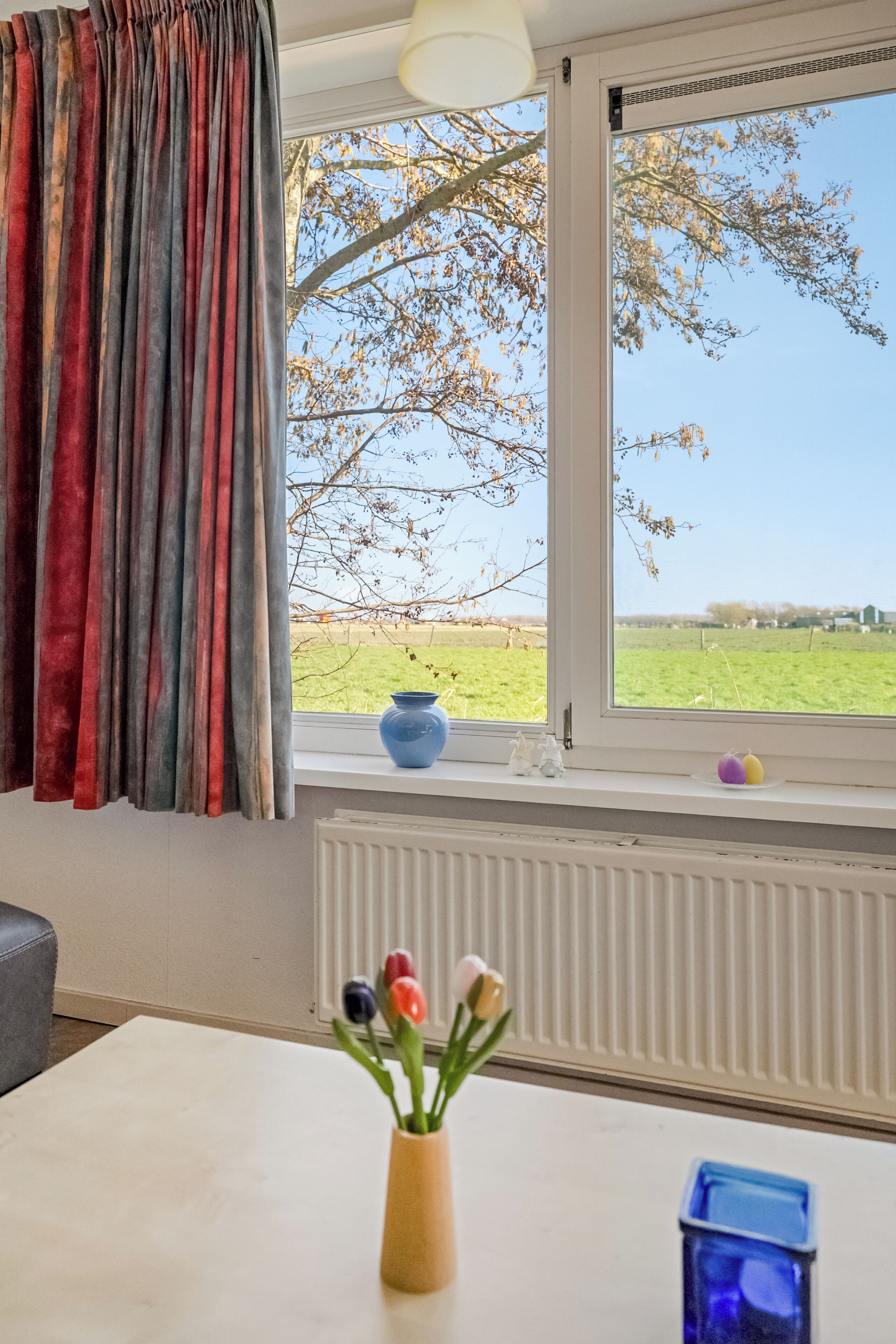 A room with a window, a radiator, a table, and a vase with flowers.