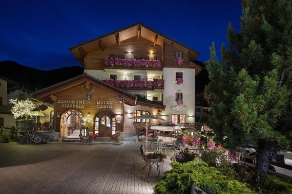 A hotel with a restaurant and pizzeria on the ground floor, featuring a wooden facade and balconies with flowers. - Hotel Cervo (Livigno)