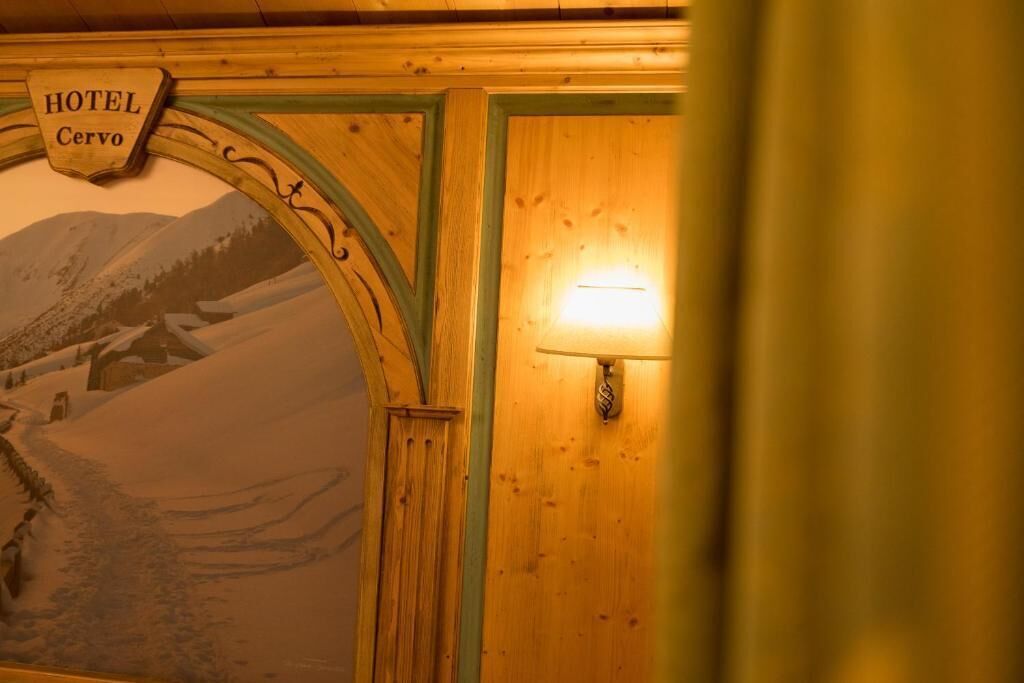 Pared de madera con un letrero que dice "HOTEL Cervo" y una lámpara.