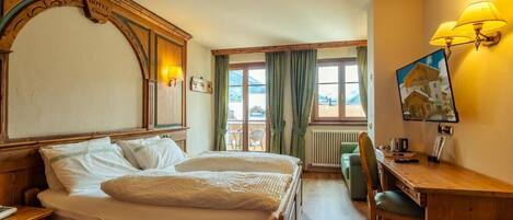 A hotel room with a wooden bed, a desk with a lamp, a chair, and a view of the mountains through the window.