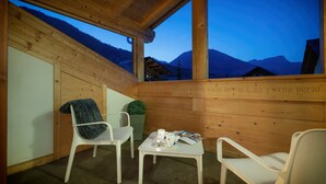 Une cabane en bois avec une table et des chaises, une petite plante et une vue sur les montagnes.