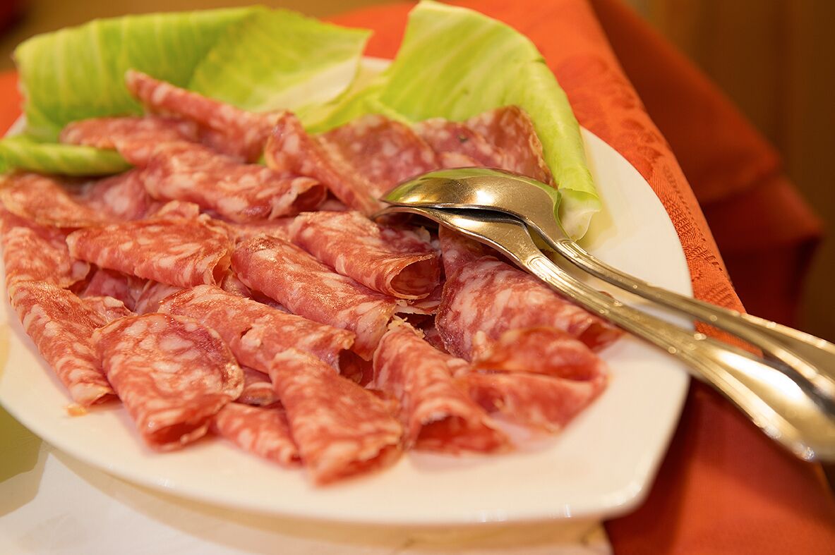 A plate of sliced cured meat with a spoon and lettuce leaves.