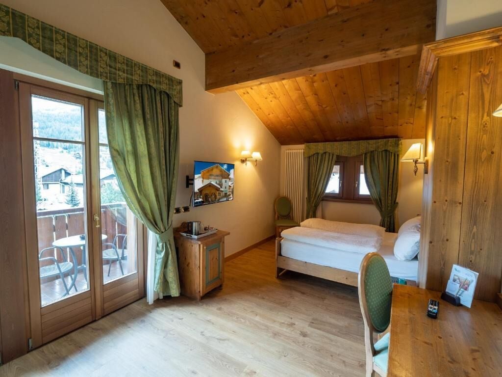A cozy room with a bed, a small table, a chair, and a view of the outside.