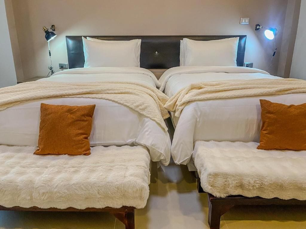 Una cama doble con ropa de cama blanca y dos almohadas marrones, una lámpara de noche y un aplique de pared.