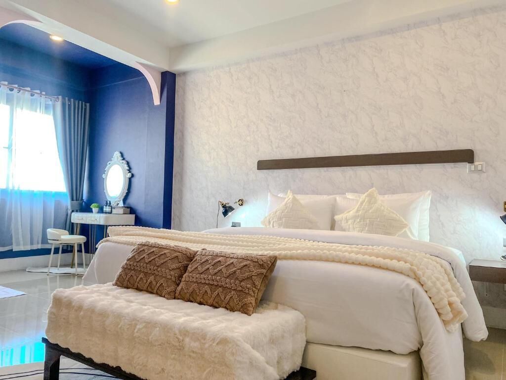 A bedroom with a large bed, a bedside table, a mirror, and a window with curtains.