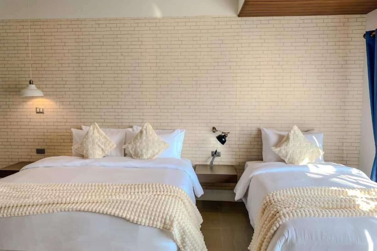 Een hotelkamer met twee bedden, witte lakens, een bakstenen muur, een houten plafond en een klein tafeltje met een lamp.