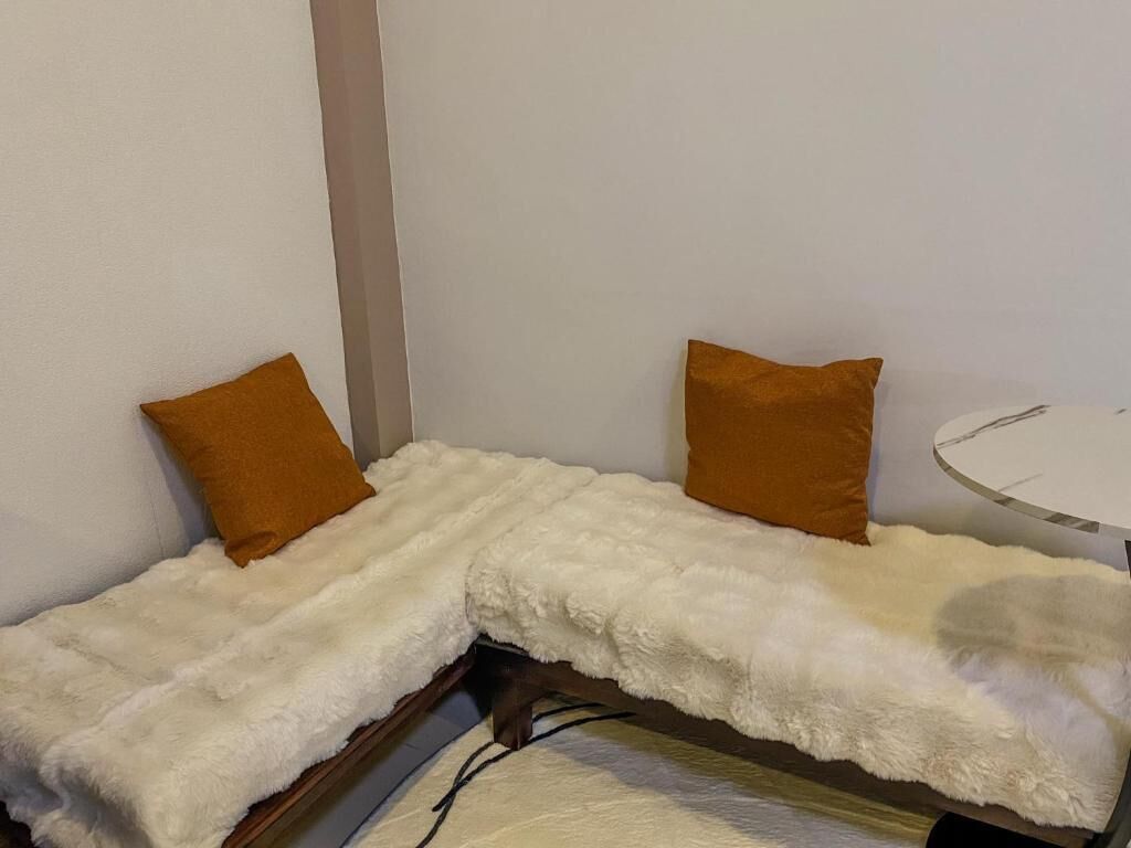 A corner room with a white furry bench, two brown pillows, and a small round table.