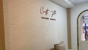 Una boutique con una pared de ladrillo blanco y un letrero que dice "Boutique Nimmam". Hay dos sofás con cojines en primer plano.