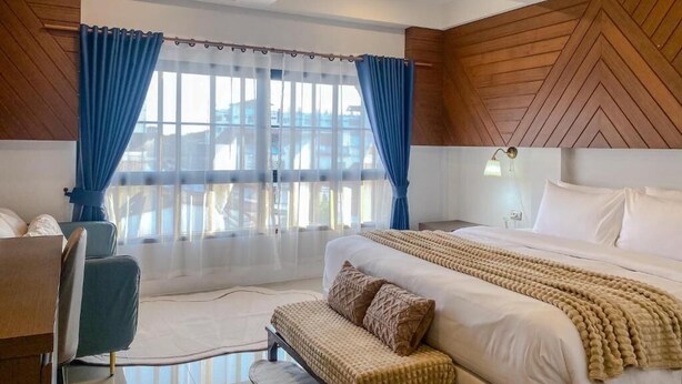 Una habitación de hotel moderna con una cama grande, un escritorio y vistas de la ciudad a través de amplios ventanales.