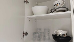 A white cabinet with shelves holding white bowls, plates, and a black bowl with a white mug. - Studio room near Koblenz (Sankt Sebastian)