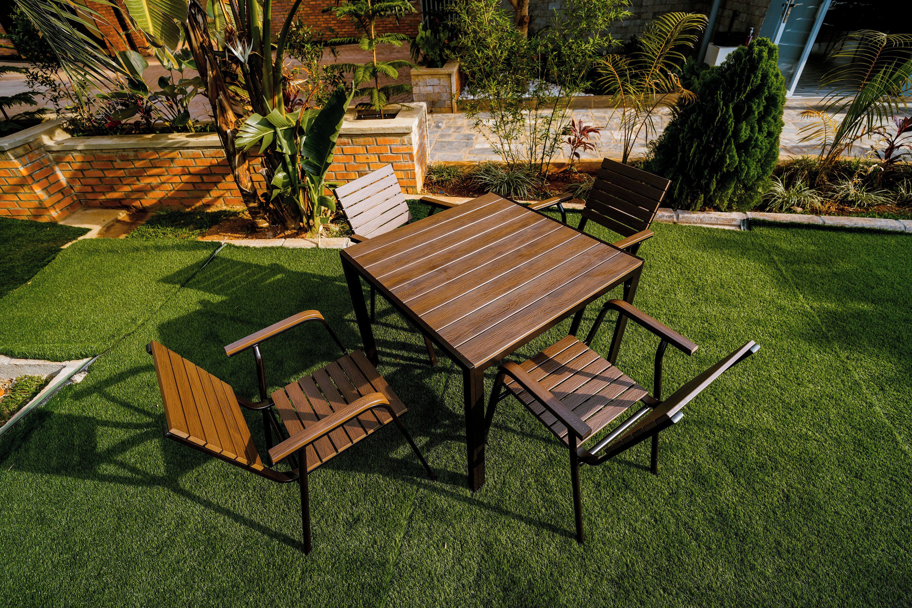 A patio with a wooden table and chairs, surrounded by well-maintained grass and plants.