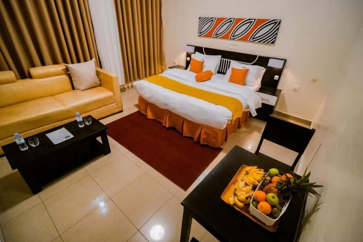 A hotel room with a bed, a sofa, a coffee table, and a fruit basket.