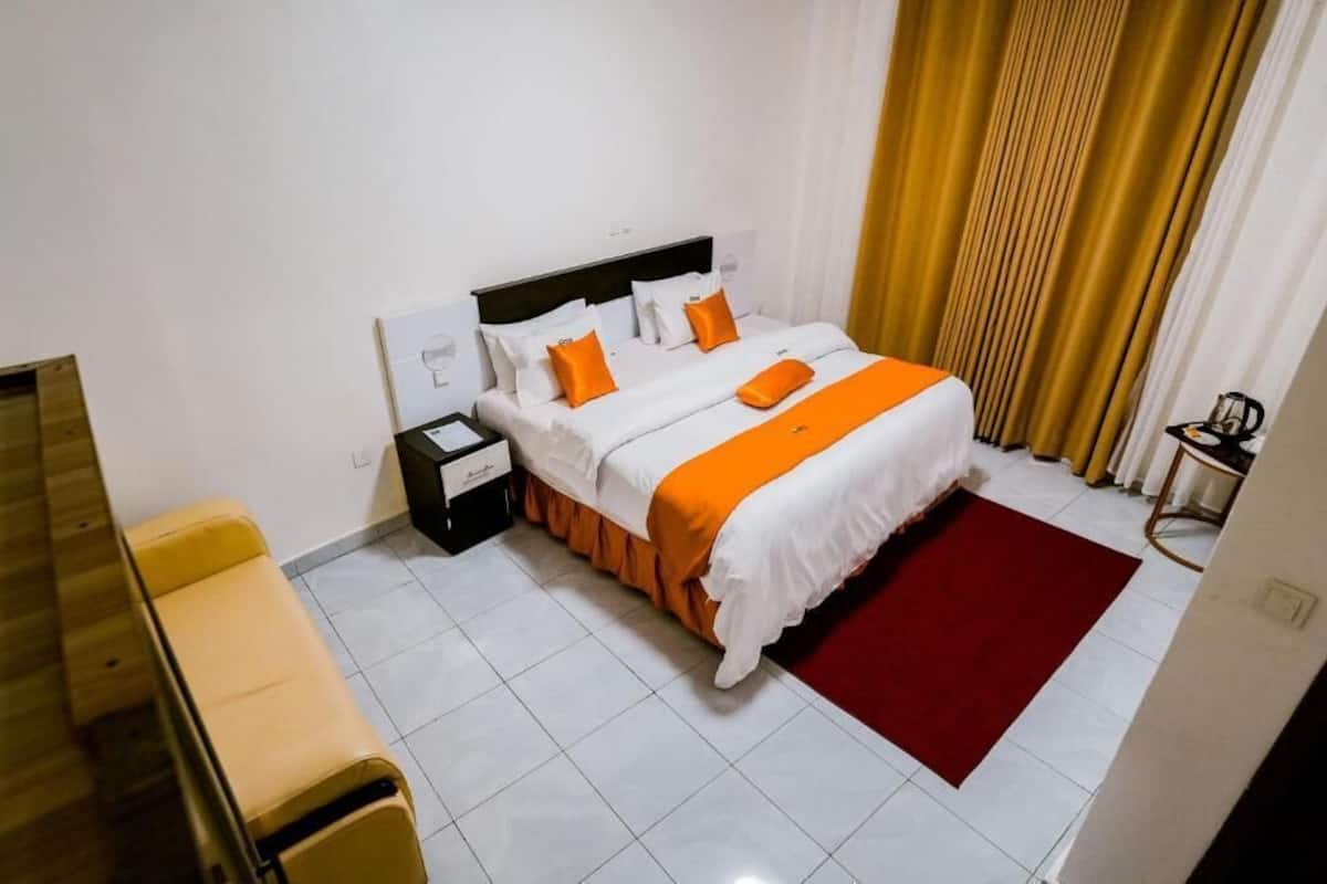 A hotel room with a bed, bedside tables, a bench, and a red rug.