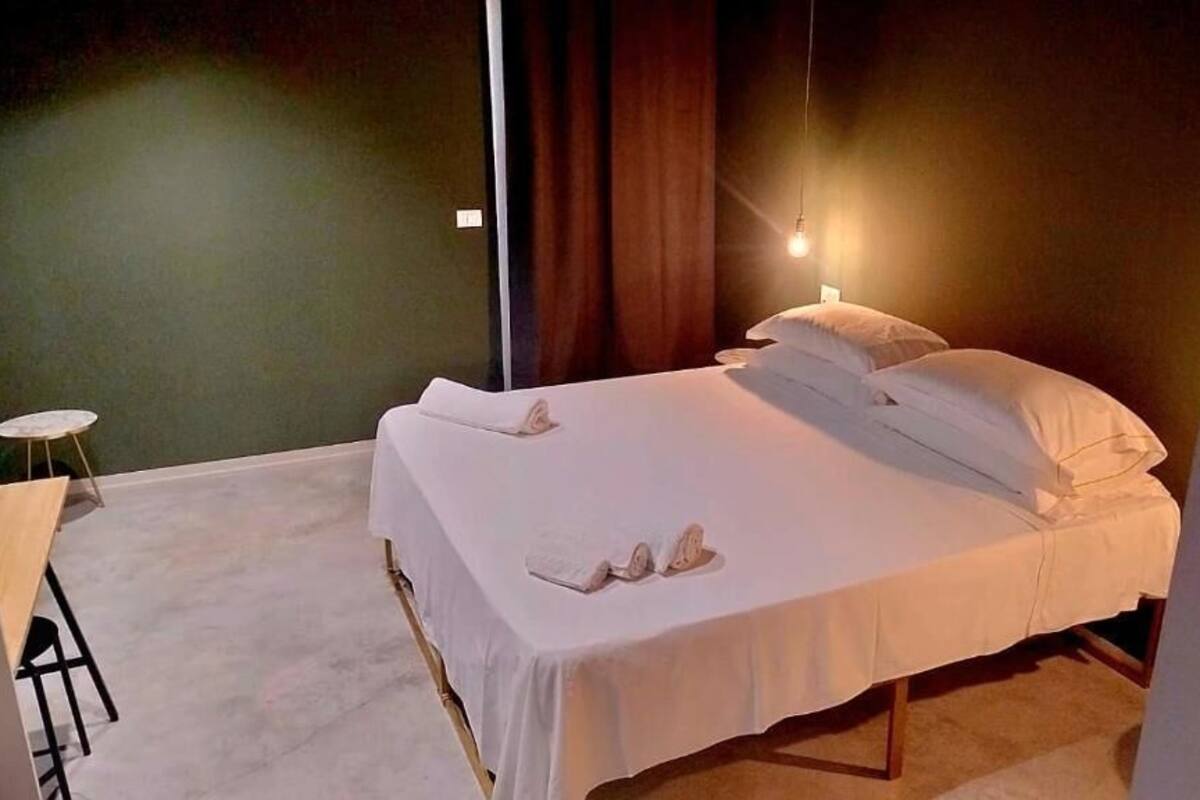 A neatly made bed with pillows and a blanket, a small round table with a chair, and a hanging light fixture.