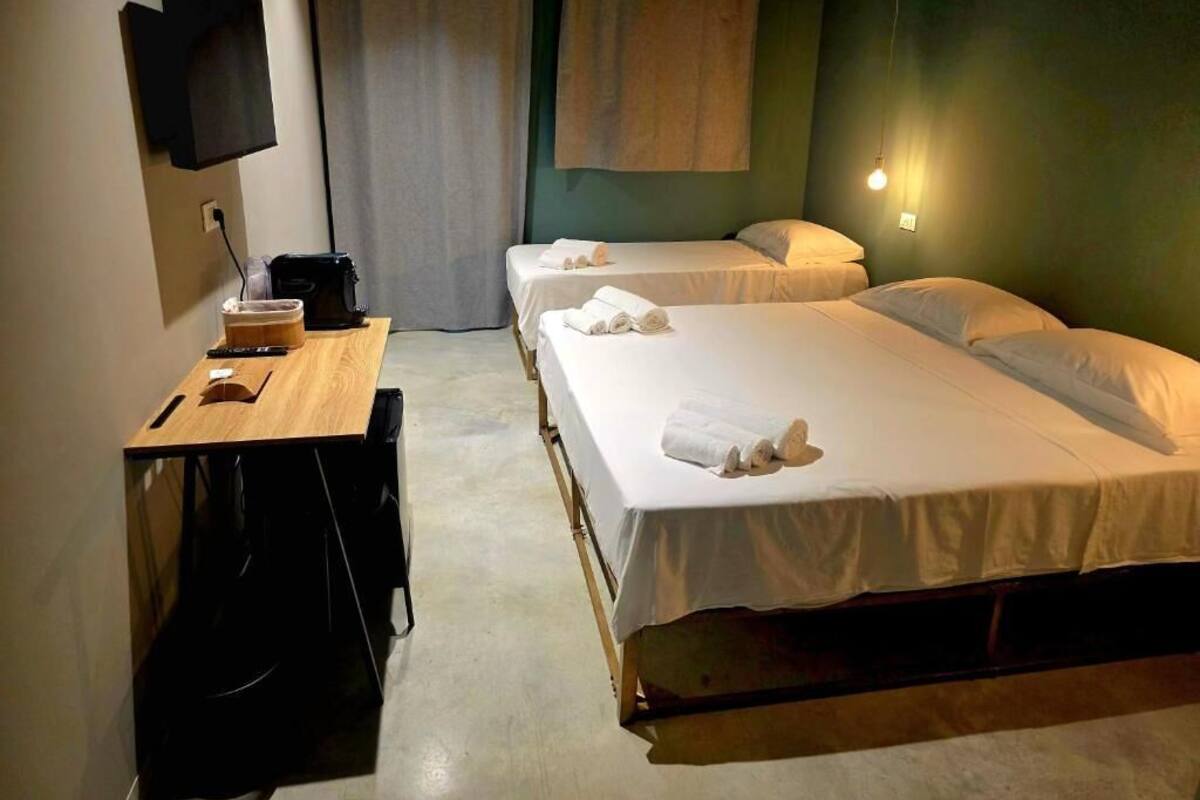 A hotel room with two beds, a desk, a chair, a TV mounted on the wall, and a window with curtains.