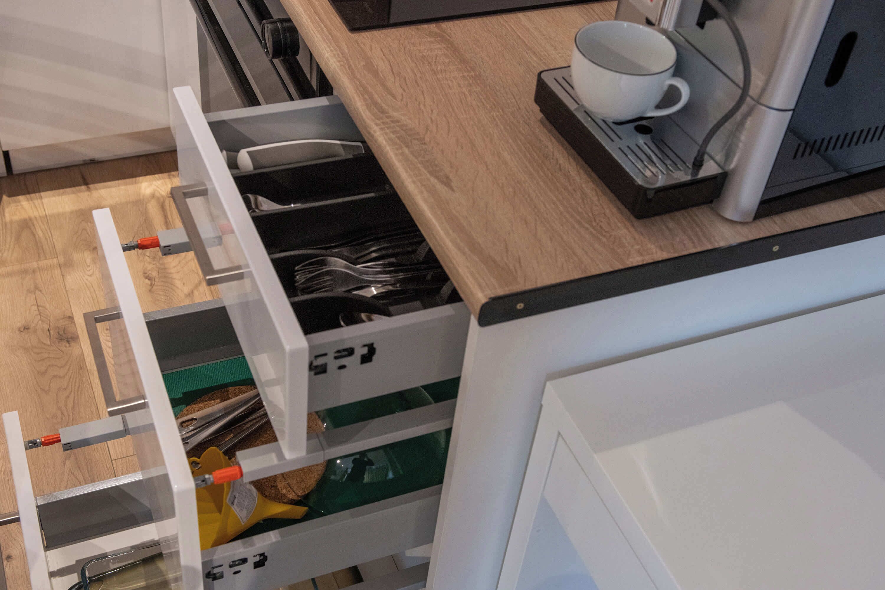 A kitchen with a wooden countertop, a coffee machine, and a drawer with utensils.