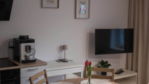 Una habitación de hotel moderna con kitchenette, televisor de pantalla plana, máquina de café, una mesa de comedor con sillas y una planta en maceta.