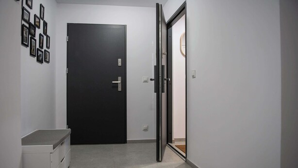 Un pasillo con una puerta negra, un armario blanco y una puerta de cristal que da a otra habitación.