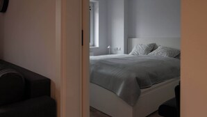 Un dormitorio con cama, mesita de noche, lámpara y ventana.