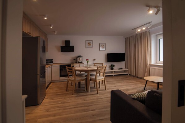A modern kitchen with wooden cabinets, a built-in refrigerator, and a dining area with a round table and chairs.