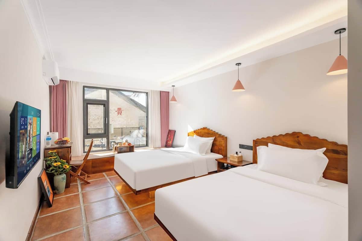Une chambre d’hôtel avec deux lits, une télévision, une fenêtre avec des rideaux et une vue sur l’extérieur.
