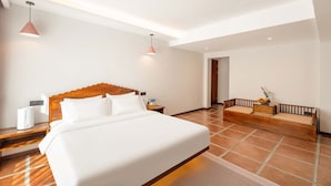 Ein Hotelzimmer mit einem großen Bett, einer Holzbank, zwei Pendelleuchten und einem Fliesenboden.